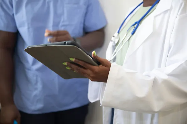 A healthcare provider holding a tablet while standing next to another professional